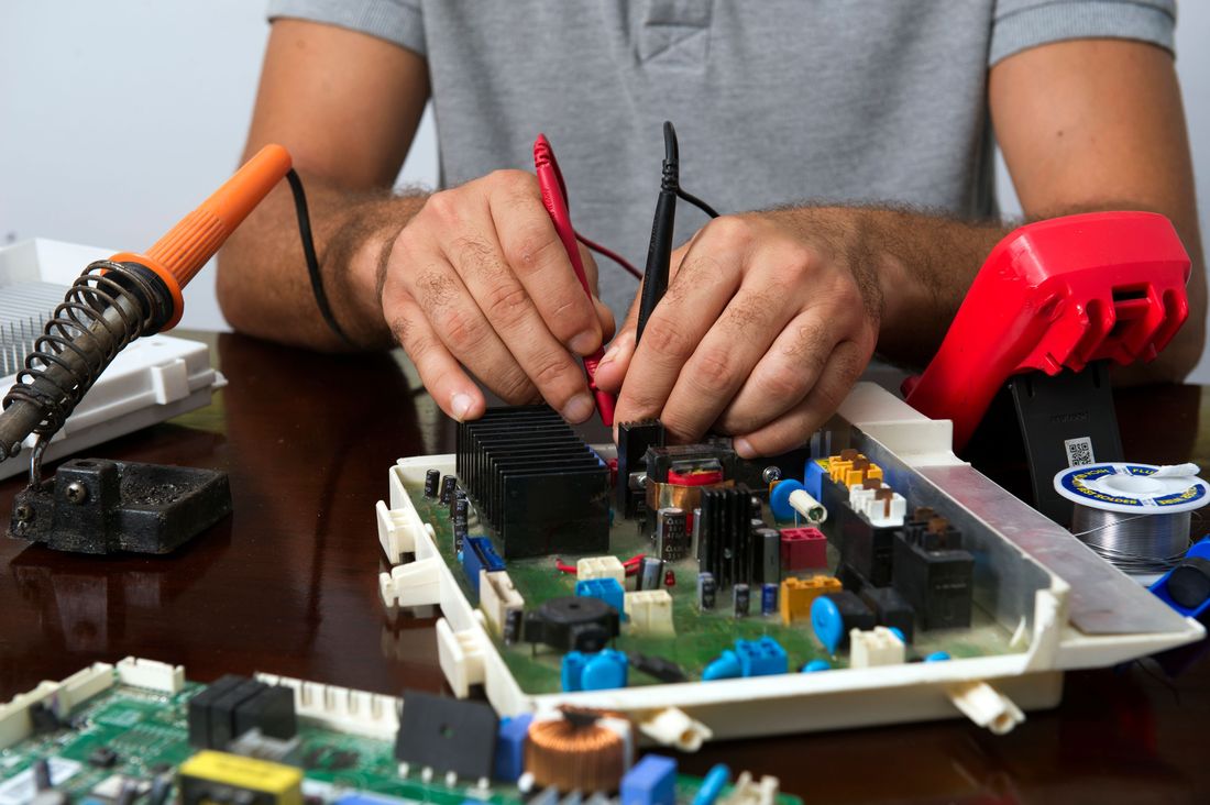 Tecnico che controlla la scheda elettronica di una lavatrice con il tester